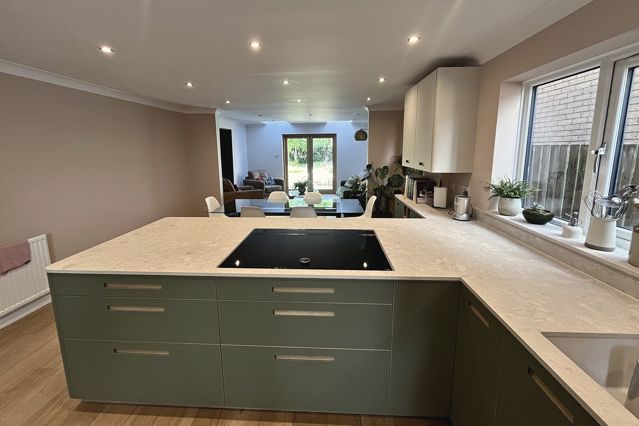 Green peninsula with black induction hob and quartz worktop looking through to garden doors