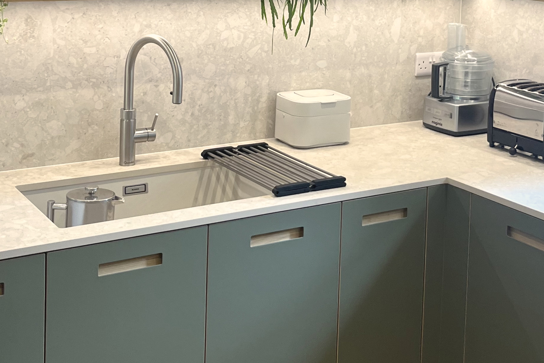 Green base units and quartz worktop with steel tap, lit oak shelf and stone splashback