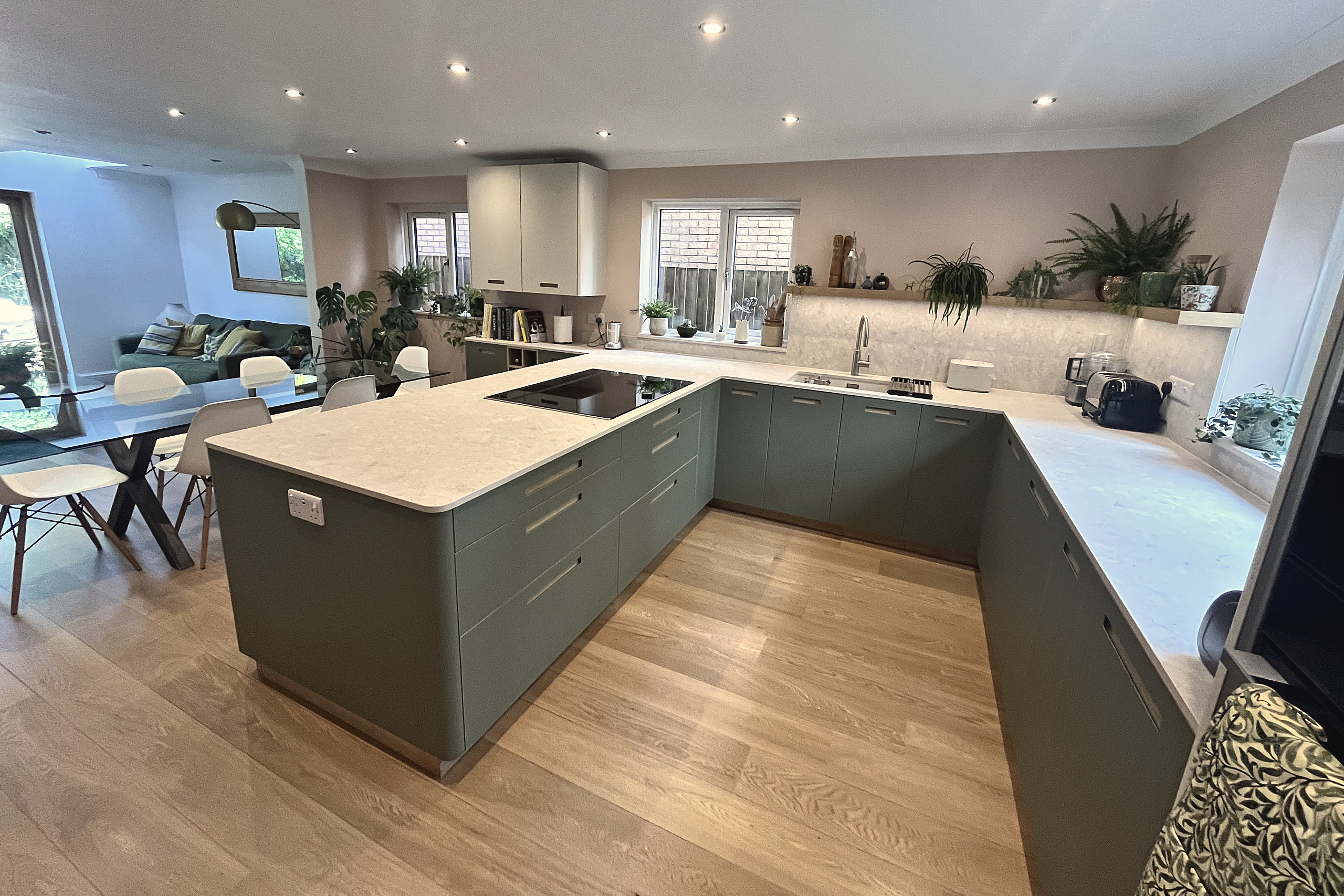 Open plan sage green kitchen with peninsula, quartz worktops and seating area beyond