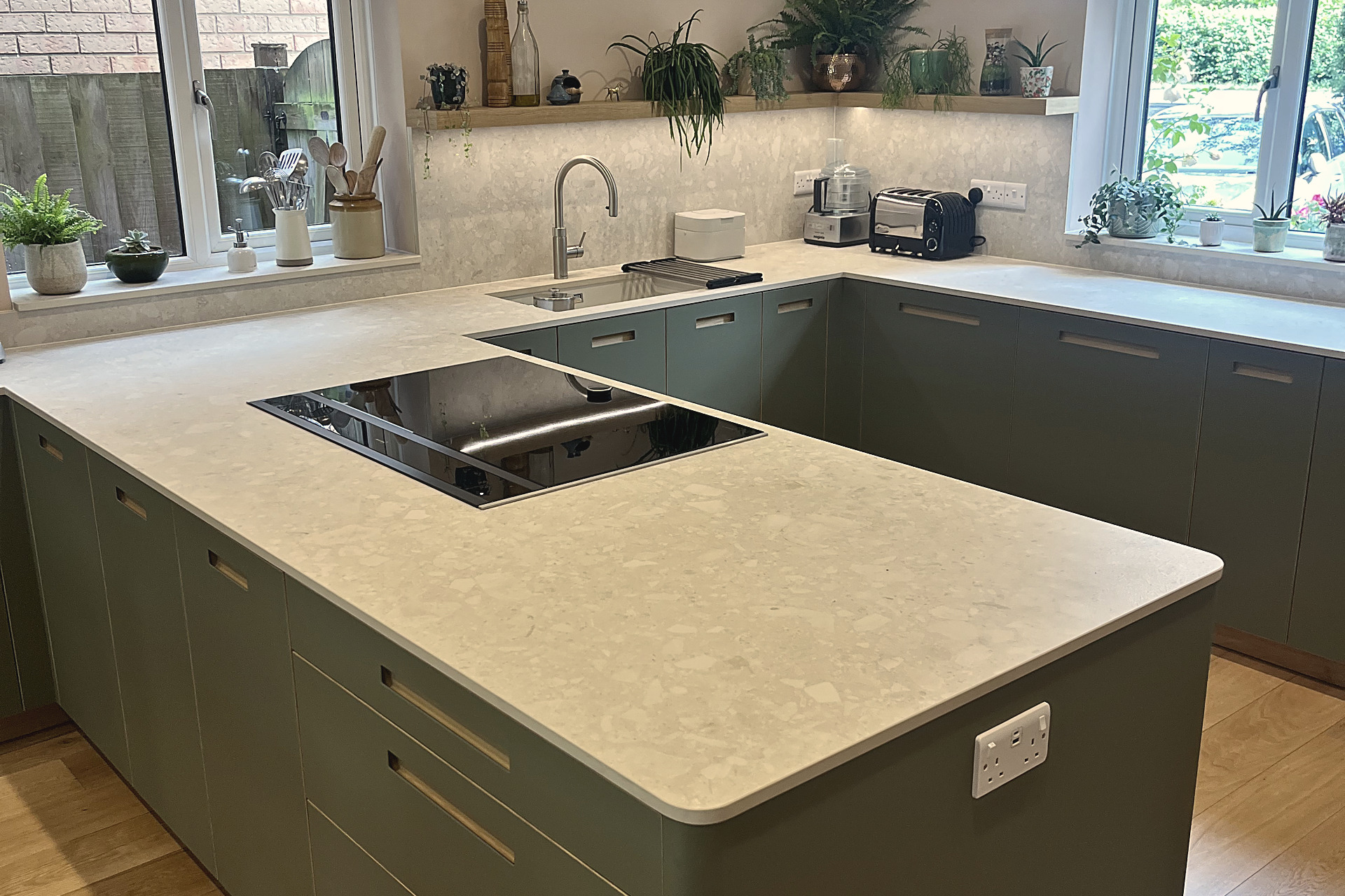 Induction hob set in pale quartz peninsula with green cabinets and stone splashback