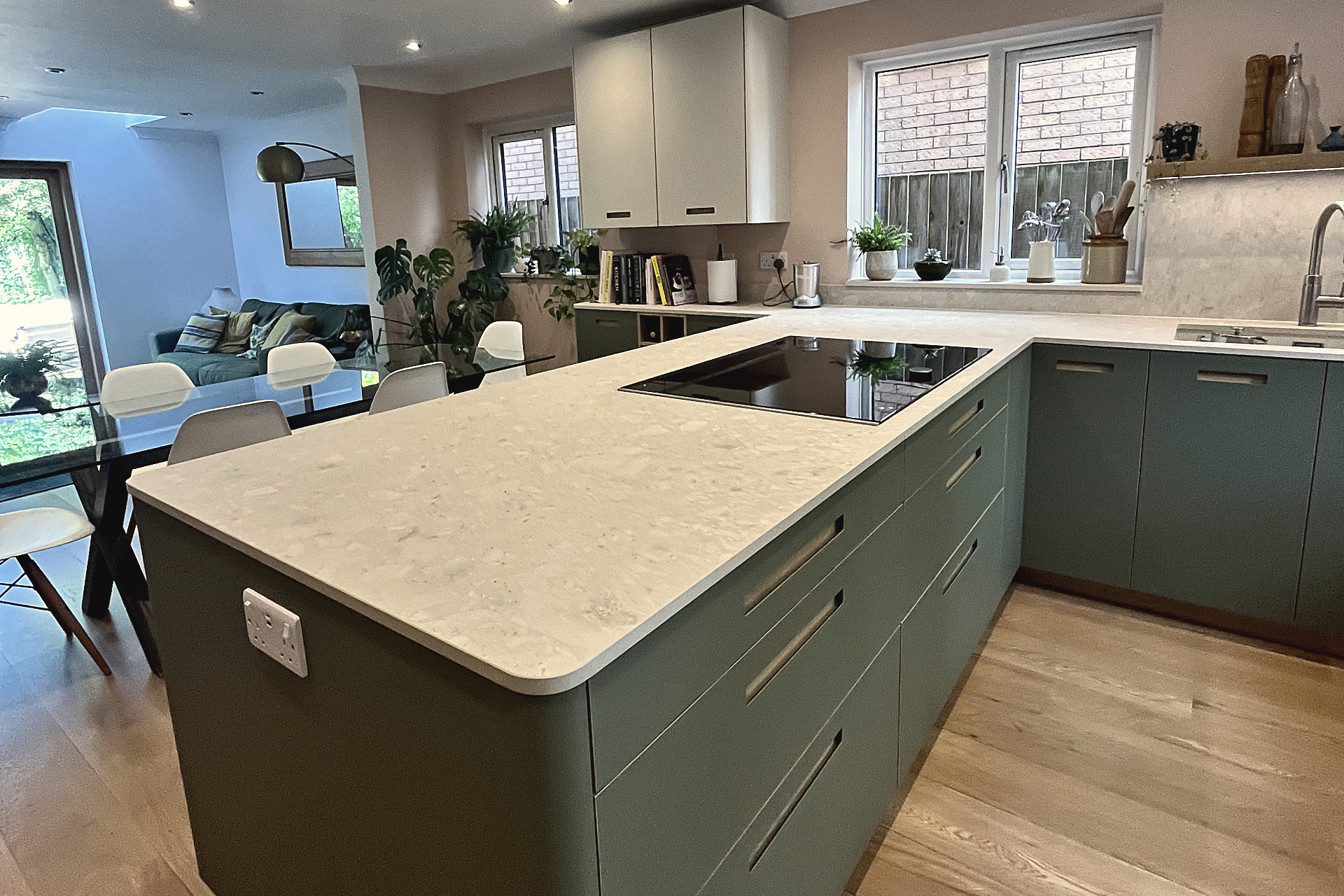 Green peninsula with pale quartz worktop and long bar handles, open to living area