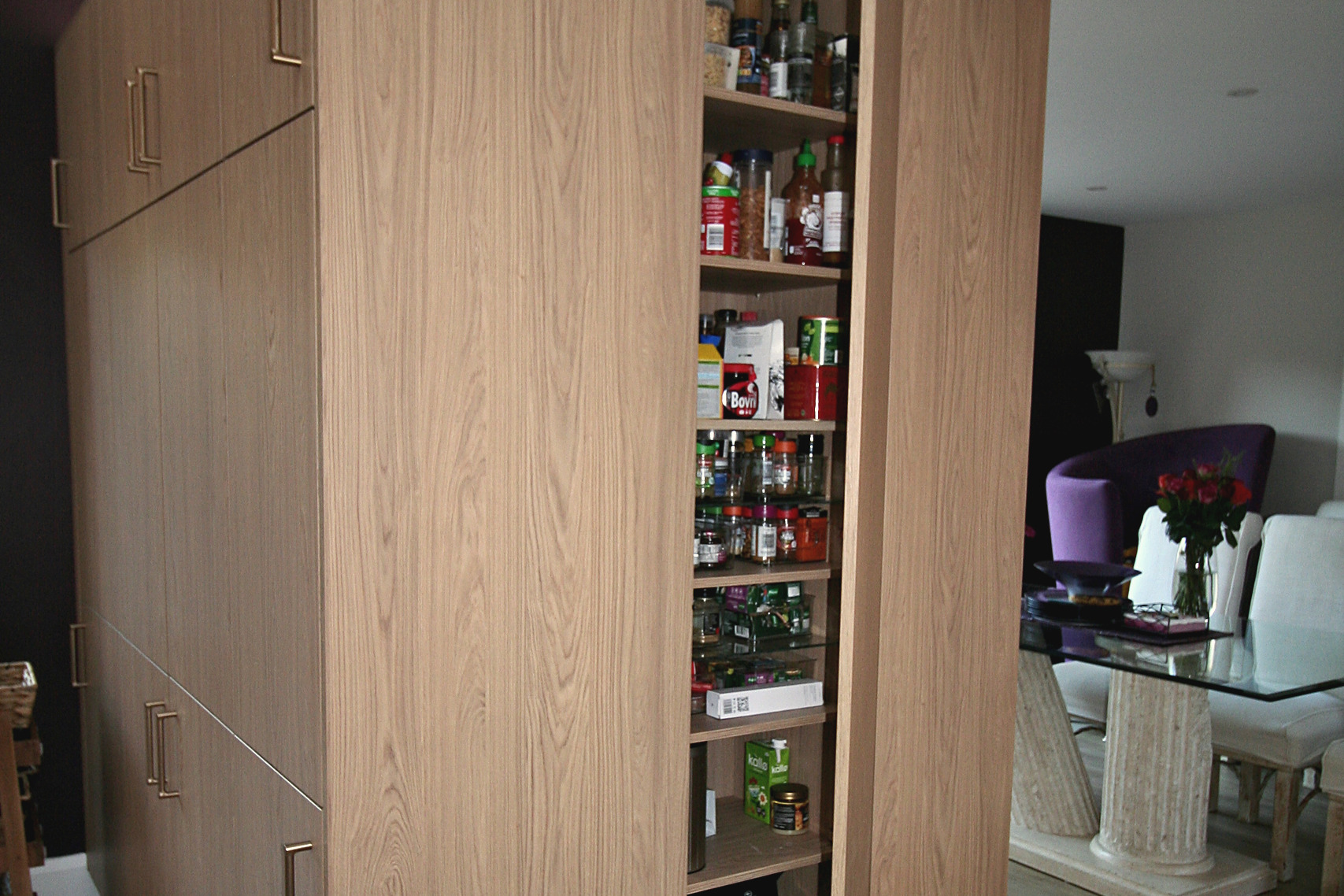 Tall oak larder unit with pull-out shelving open to show stacked food storage