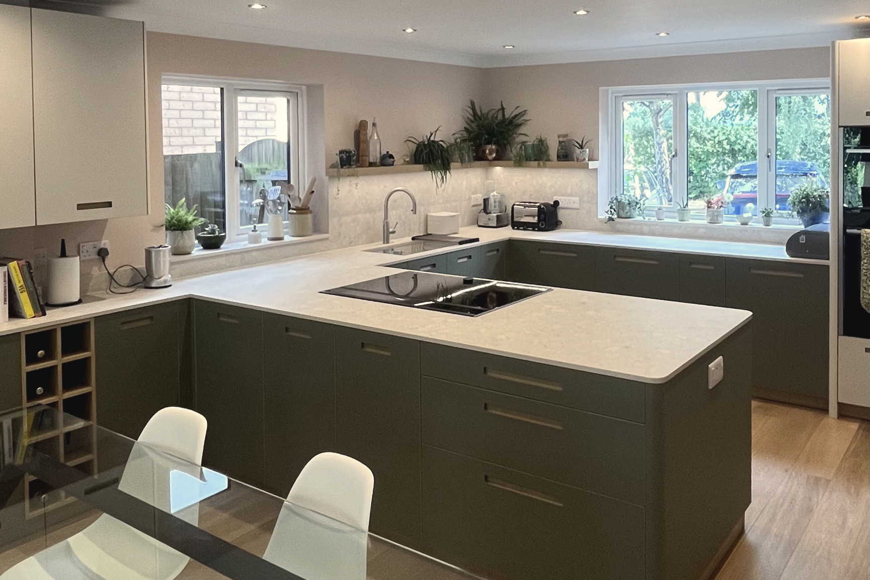 Sage green kitchen with quartz worktops, wine rack and glass dining table in foreground