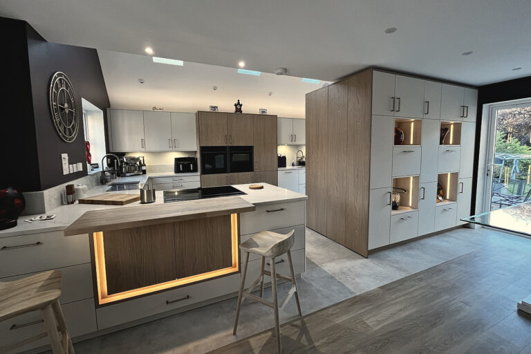 Open-plan kitchen with pale grey handleless units, oak tall cabinets and a lit oak breakfast bar island