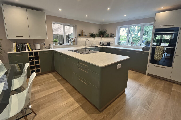 Sage green kitchen with pale quartz worktops, wine rack, built-in ovens and oak flooring