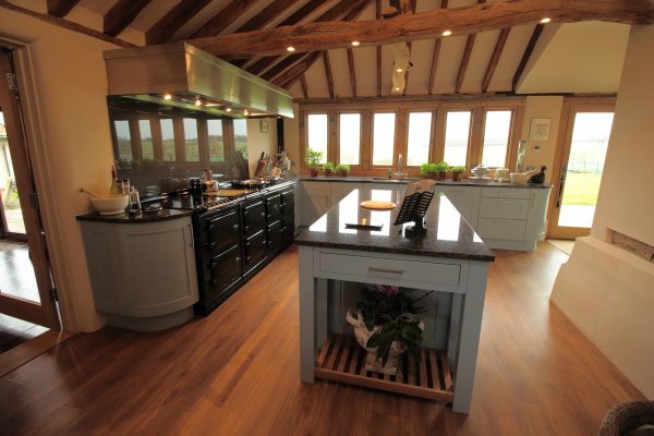 Barn conversion kitchen with exposed beams, a vaulted ceiling, an island and a black range cooker
