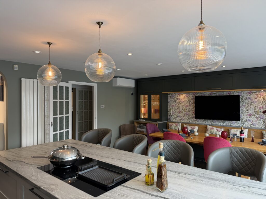 A fitted kitchen island under three glass pendants, looking through to banquette seating and a dining table