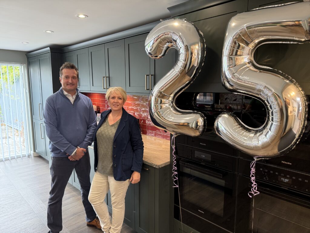 Two of the Kitchensmiths team beside silver 25 balloons in the Histon showroom
