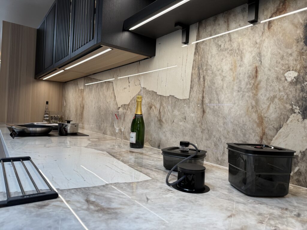 A quartzite worktop and full-height splashback under black slatted wall units, with downdraft extraction set into the surface