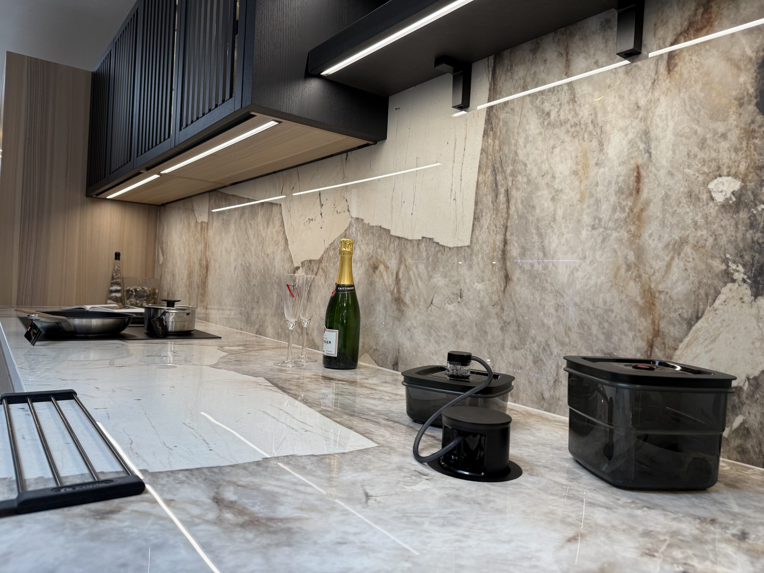 A quartzite worktop and full-height splashback under black slatted wall units, with downdraft extraction set into the surface