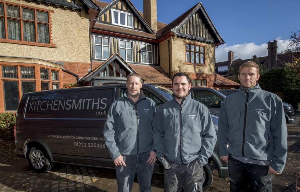 Three Kitchensmiths fitters in branded jackets in front of a branded van, outside a house