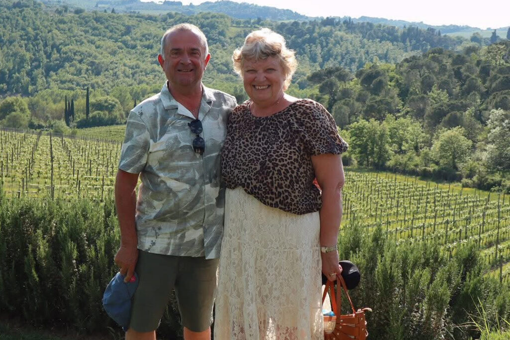 Martin and Debra Smith standing together in a vineyard on a bright day, the hillside rows behind them