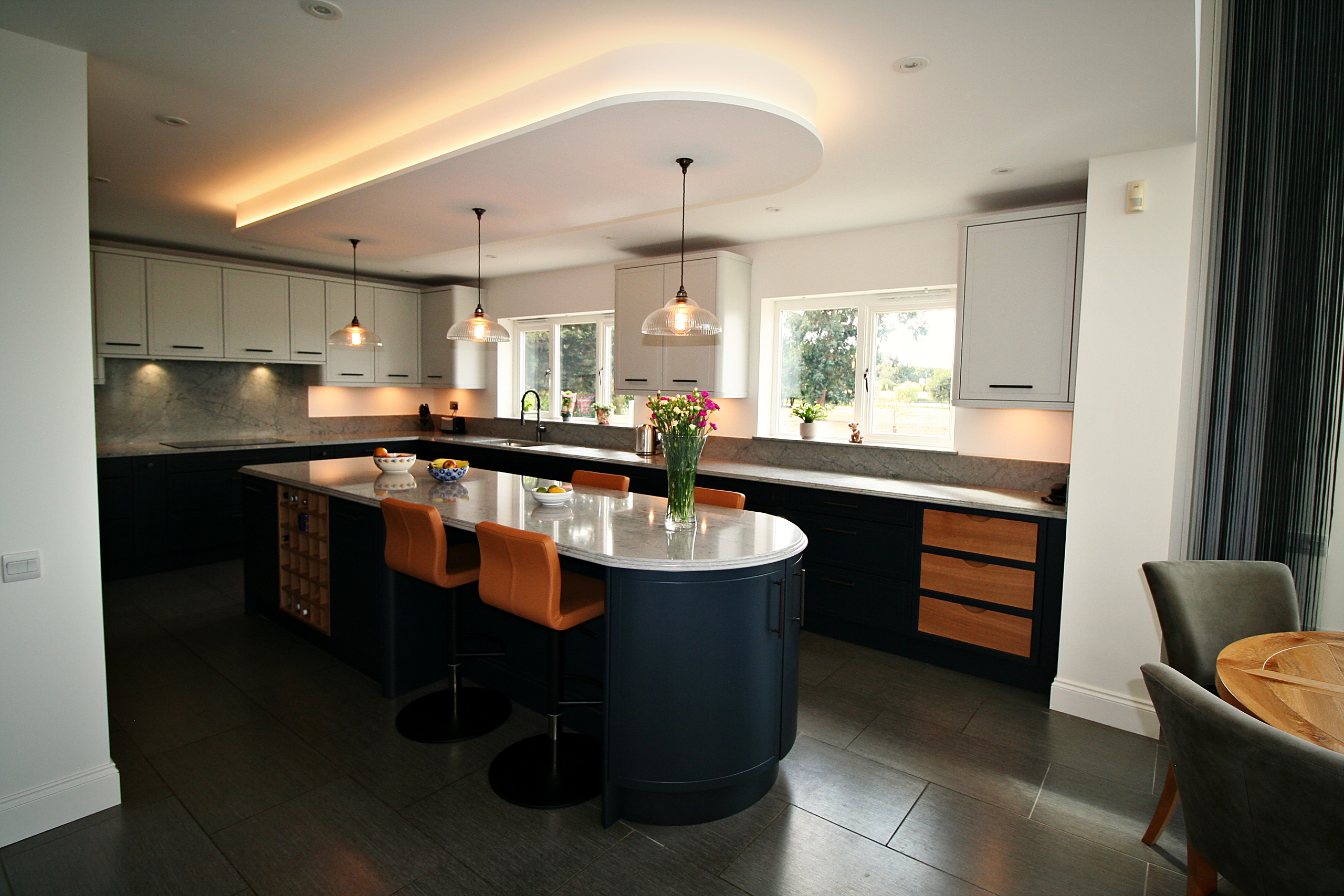 Railings painted island with fluted bronze handles beneath glass pendants and an illuminated ceiling recess