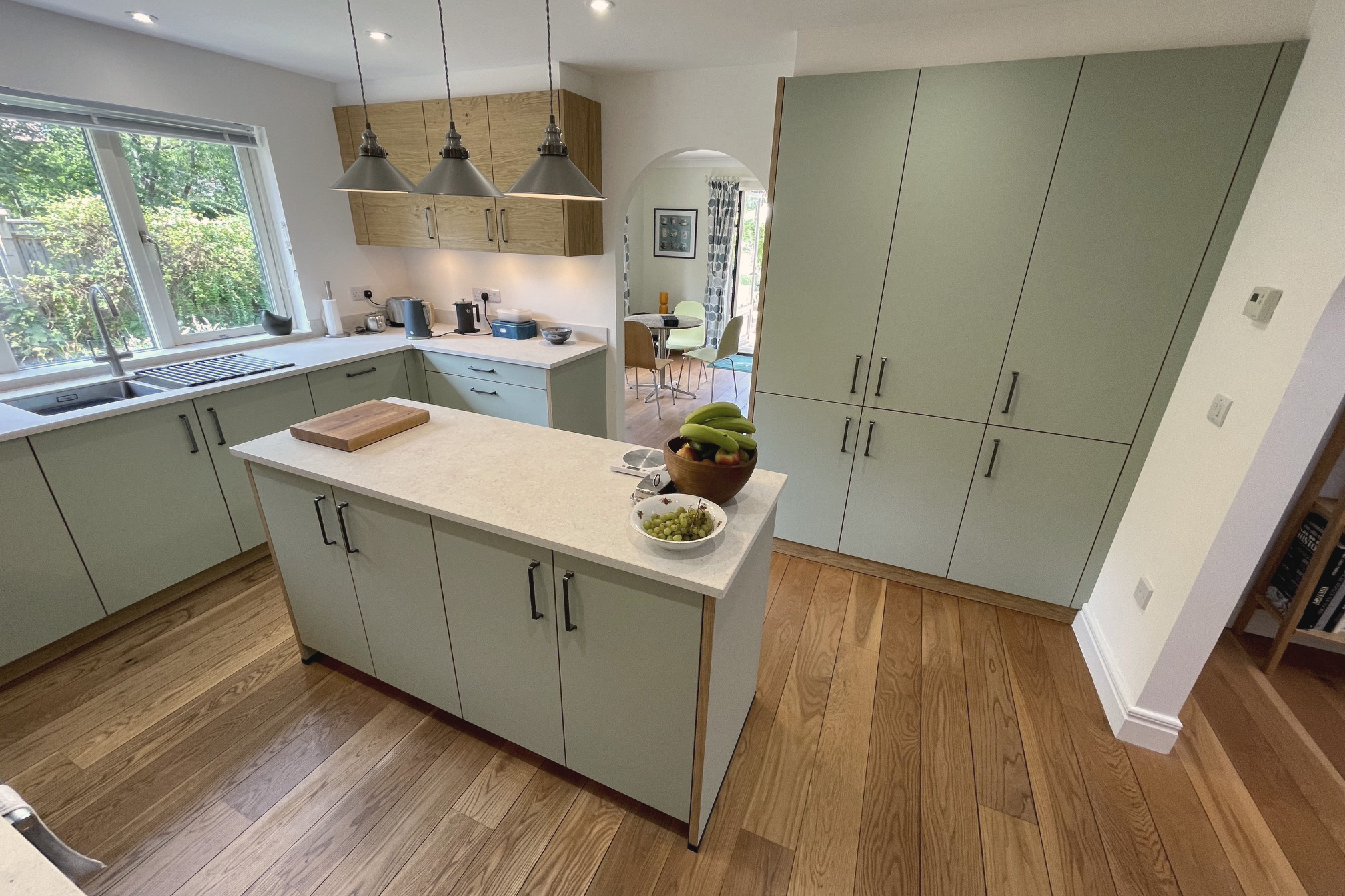 Quartz-topped sage green island with steel pendants and a floor-to-ceiling bank of matching tall units